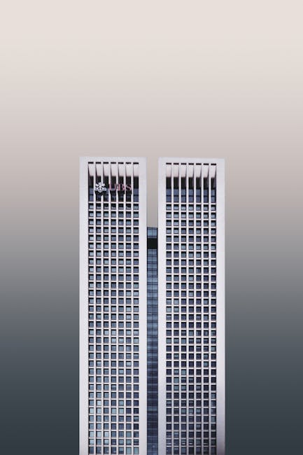 A modern twin skyscraper with a minimalist facade against a neutral sky.
